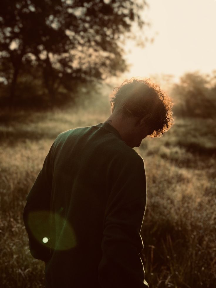 A man with curly hair walks through tall grass at sunrise, the low sun lighting his hair from behind.