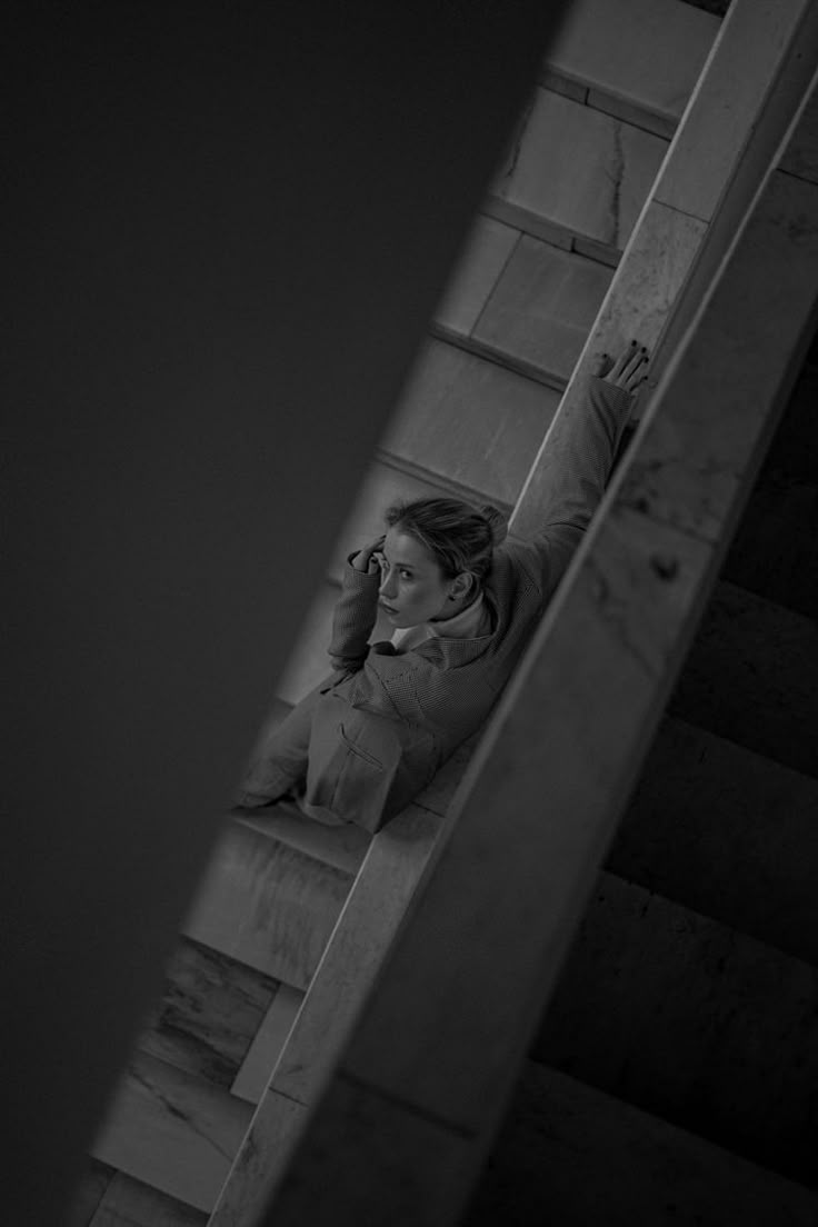 Black and white, seen from above: a woman leans back on a marble stair rail, one hand in her hair.